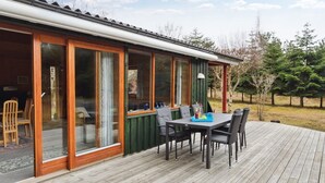 A wooden deck with a table and chairs, a covered outdoor area with sliding glass doors, and a view of a forested area. - "Nada" - 200m from the sea by Interhome (Aakirkeby)
