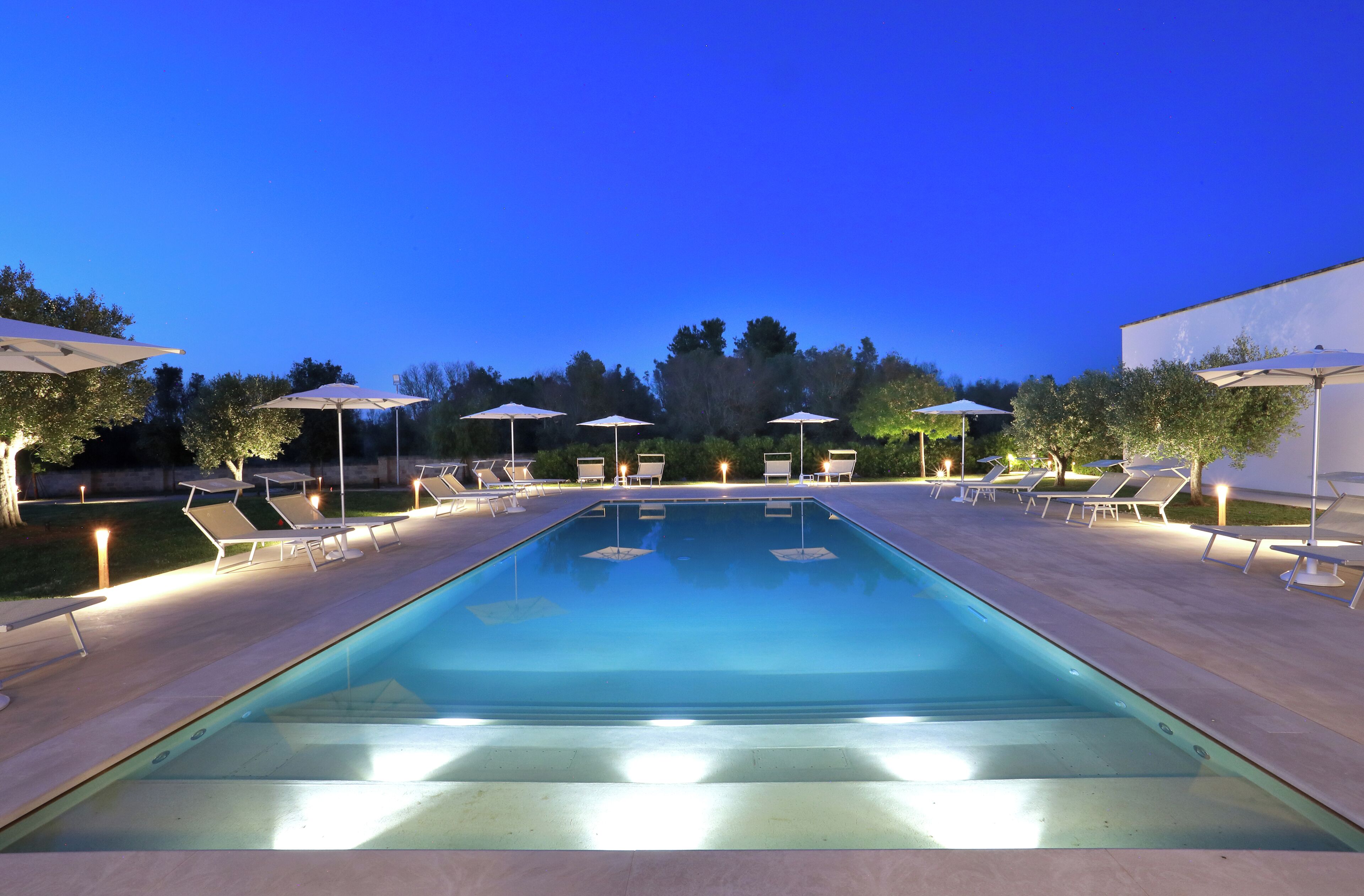 Ein rechteckiger Pool mit mehreren Liegestühlen und Sonnenschirmen darum herum.