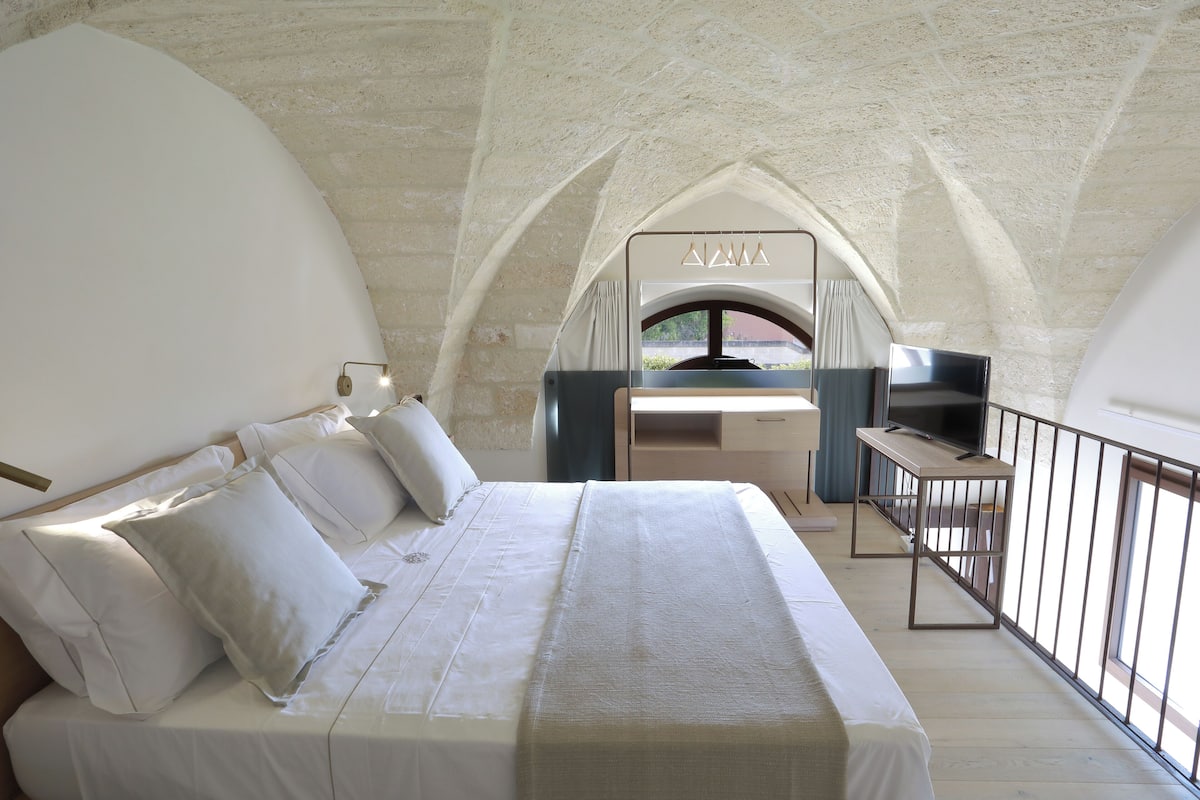 A bedroom with a large bed, a desk, and a TV.