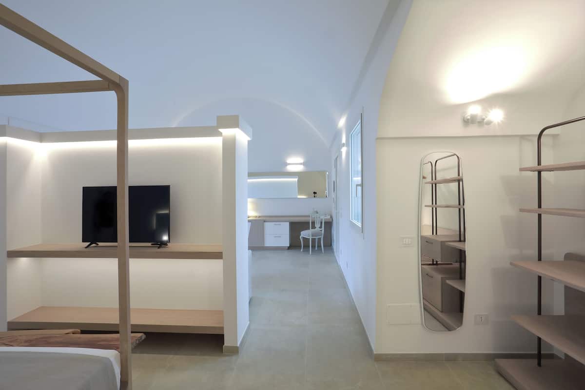 A modern hotel room with a TV, a desk, a chair, and built-in shelves.