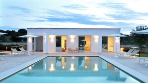 Ett modernt hus med pool, utomhusmöbler och stora parasoller.