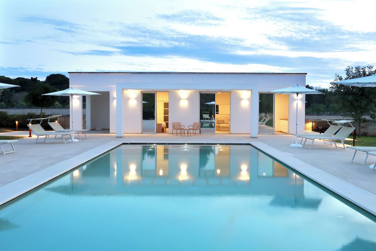 A modern house with a pool, outdoor seating, and large umbrellas.