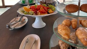 En frukostbuffé med frukt, bakverk och utsikt över grönskan utanför.