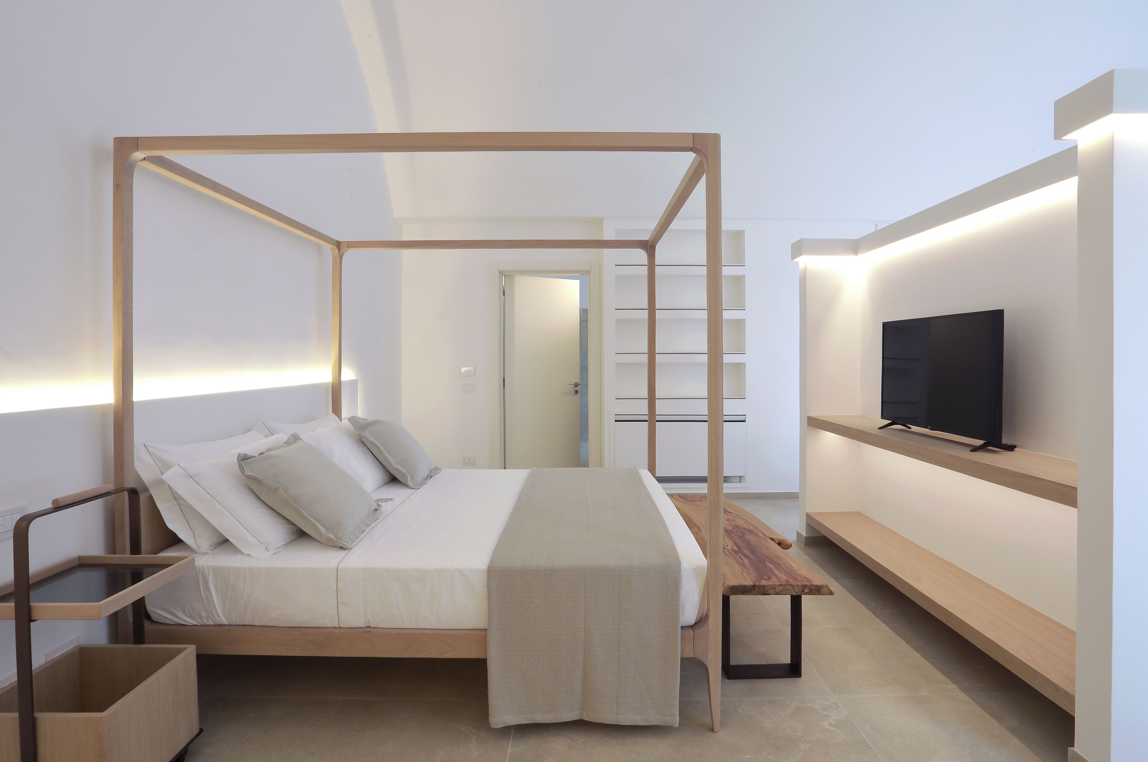 A modern bedroom with a four-poster bed, a television on a shelf, and a minimalist design.