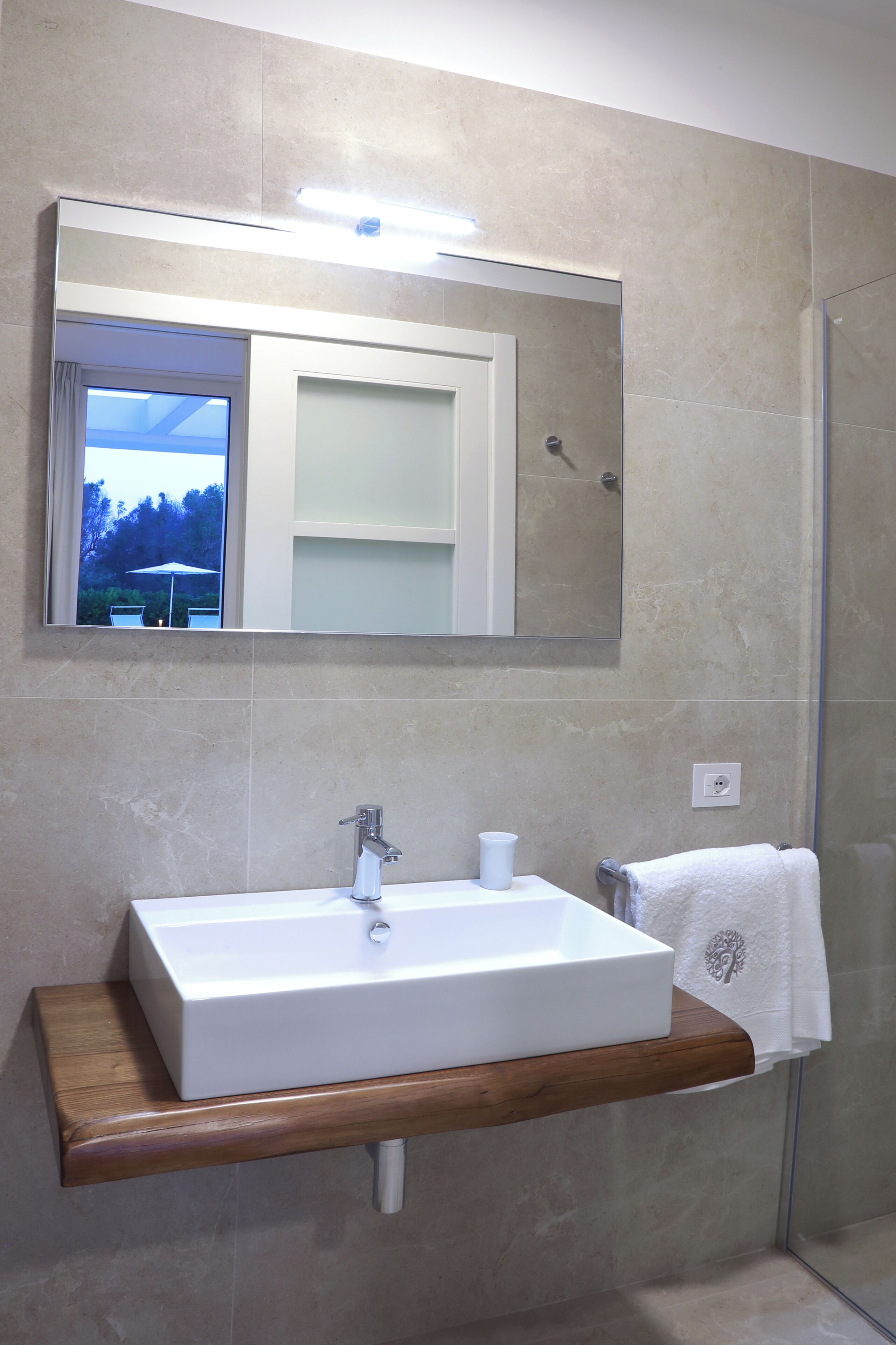 A bathroom with a rectangular sink, a mirror above it, and a shower to the right.