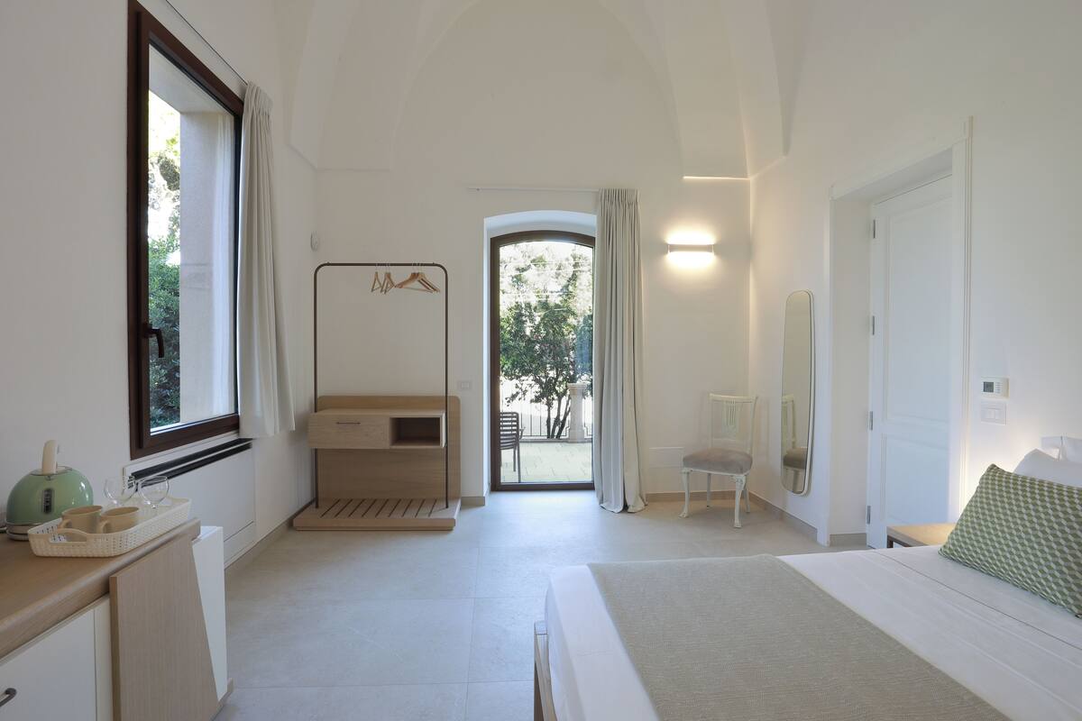 A bedroom with a bed, a bedside table, a chair, a window, and a door.
