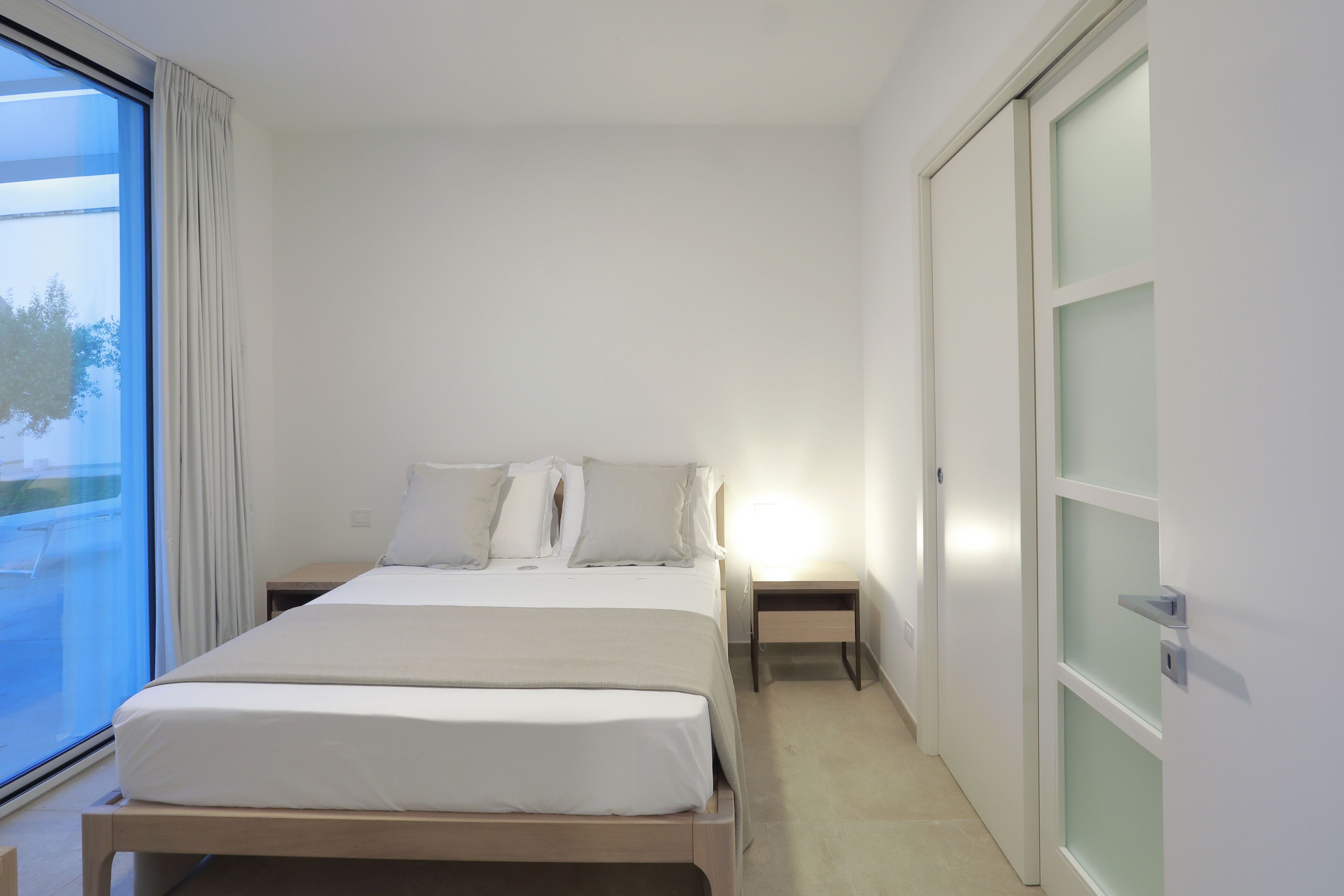 A minimalist bedroom with a bed, bedside tables, and a sliding door.