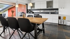 Een moderne keuken met witte kasten, een eettafel met stoelen en hanglampen.