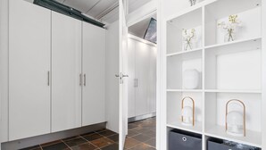 Een moderne kamer met witte kasten, een witte open plankenwand met decoratieve items, en een betegelde vloer.