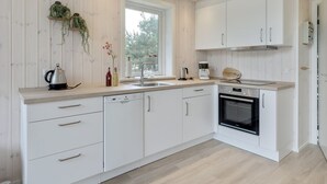 Une cuisine moderne avec des meubles blancs, un four encastré et une fenêtre donnant sur un paysage verdoyant.