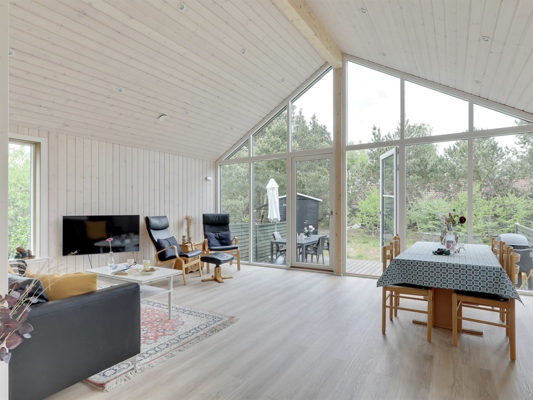 A spacious living area with a large TV, comfortable seating, and a dining table with a view of the outdoors.