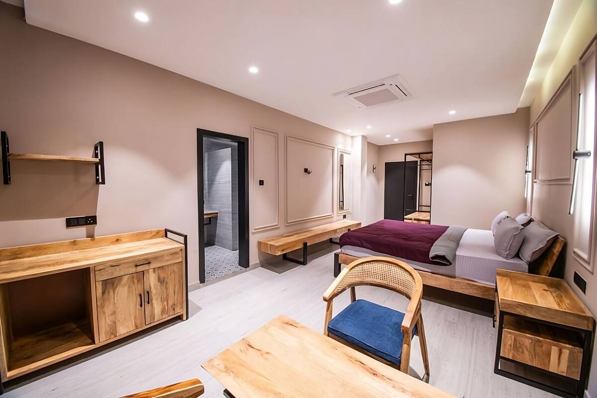 A modern hotel room with a bed, a desk, a chair, and a wardrobe.