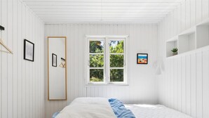 Ein Schlafzimmer mit Bett, Fenster, Spiegel und Wandregal.