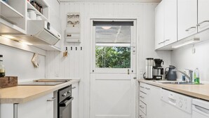 Eine kleine Küche mit weißen Schränken, einem Einbauofen, einer Kaffeemaschine und einem Spülbecken.