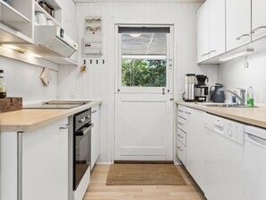 Una cucina compatta con mobili bianchi, forno integrato, macchina da caffè e lavello.