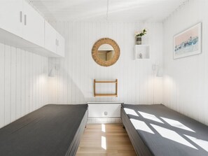 Une pièce au décor minimaliste, avec un plancher en bois, un miroir rond, une petite étagère ornée d’une plante et un tableau encadré accroché au mur.