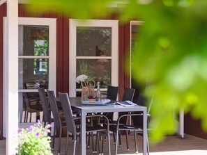 Un'area pranzo all'aperto con tavolo e sedie, una bottiglia di vino e un cesto di fiori.