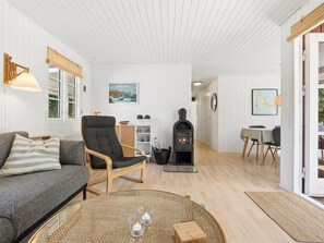 Un salon chaleureux avec un canapé, un fauteuil et une table ronde décorée de bougies. On aperçoit également une cheminée et un coin repas à l’arrière-plan.