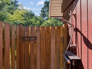 Een houten hek met een metalen poort, een slang op een muur, en een houten constructie aan de rechterkant.