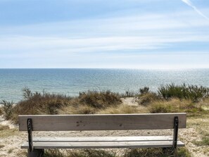 A wooden bench facing a beach with sand dunes and the ocean in the background.