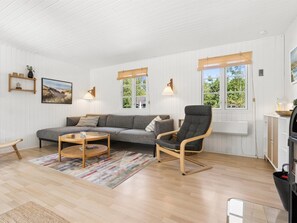 Una sala moderna con un sofá, una mesa de centro redonda, un sillón y una alfombra. Hay ventanas con cortinas, lámparas de pared y un cuadro en la pared.