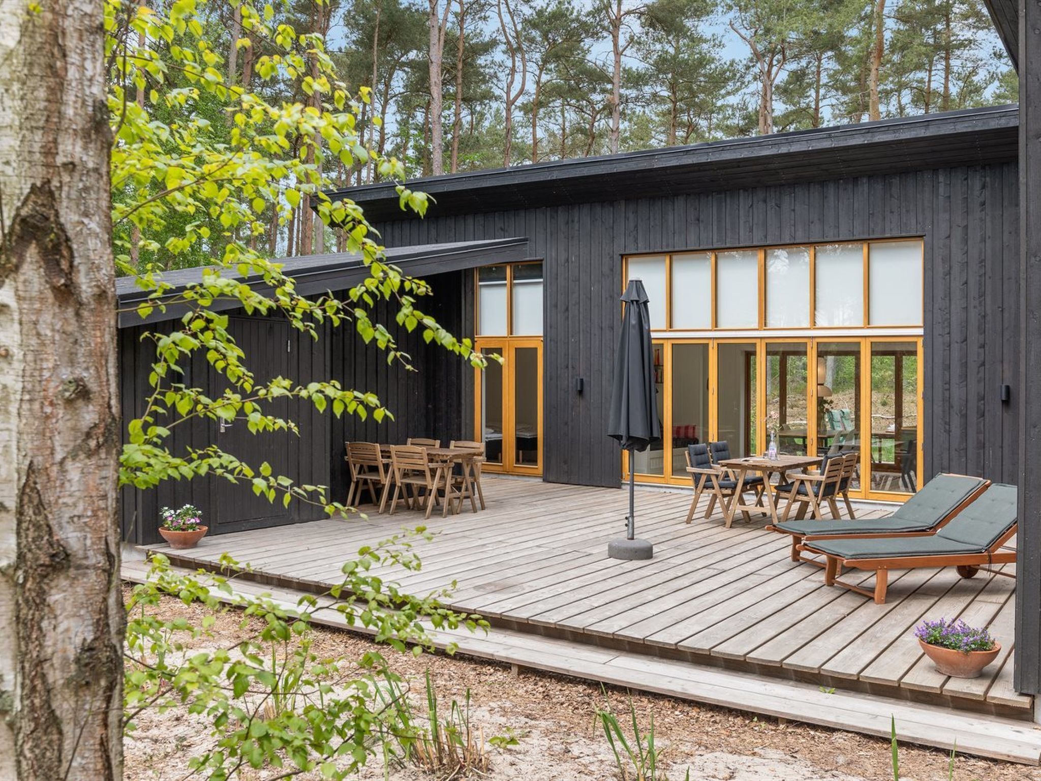 Et moderne træhus med terrasse, udendørs møbler og store glasdøre.