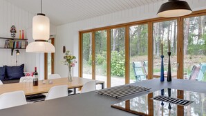 A modern kitchen with large windows, a dining area with white chairs, and a central island with a built-in range hood. - "Nuka" - 800m from the sea by Interhome (Aakirkeby)