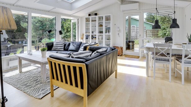 A spacious living room with a large sofa, a dining table with chairs, and a bookshelf. There are skylights on the ceiling, and the room has large windows. - "Essi" - 300m from the sea by Interhome (Aakirkeby)