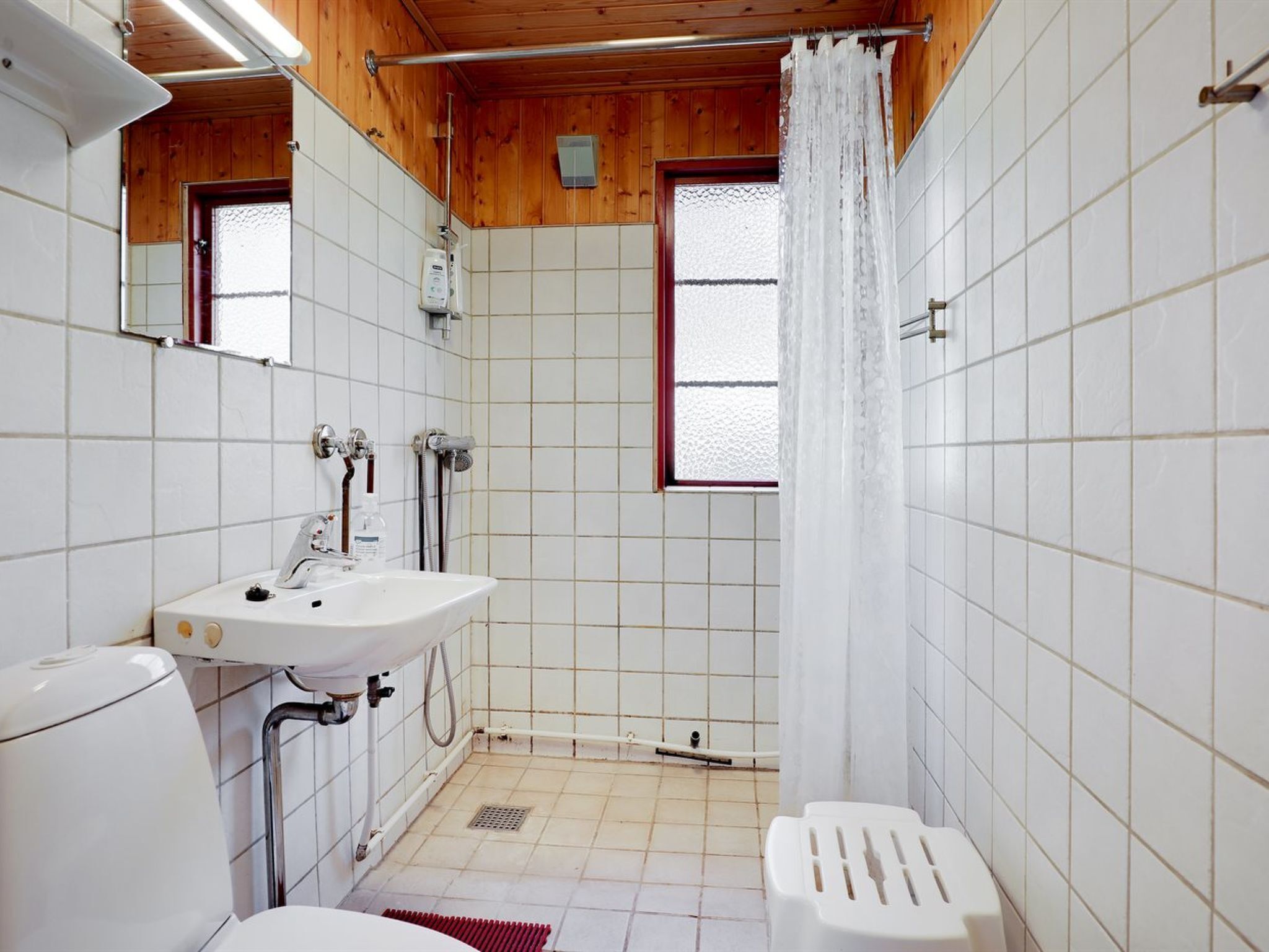 Une salle de bain compacte avec un lavabo, des toilettes et une douche, le tout agrémenté de murs en bois et d’un sol carrelé.