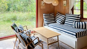 A cozy room with a wooden ceiling, a large window, a sofa with striped cushions, a wooden table, and two chairs. - "Chenoa" - 200m from the sea by Interhome (Aakirkeby)
