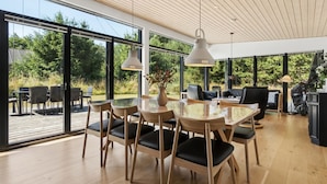 Un comedor moderno con una mesa de vidrio, sillas de madera e iluminación colgante.