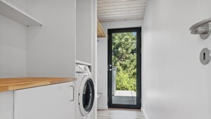 Un moderno cuarto de lavado con lavadora y secadora integradas, encimera de madera y una puerta que da a un área exterior con árboles.