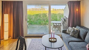 Een moderne woonkamer met een bank, een salontafel en uitzicht op een tuin en gebouwen door een schuifdeur.