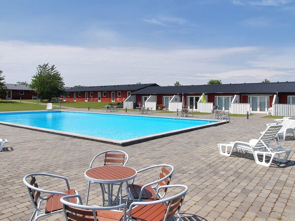 Une piscine entourée de chaises longues et de tables, le tout bordé par un bâtiment à la façade rouge et doté d’un patio couvert.