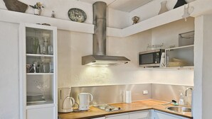 Een compacte keuken met witte kasten, een roestvrijstalen afzuigkap, een magnetron en een spoelbak.