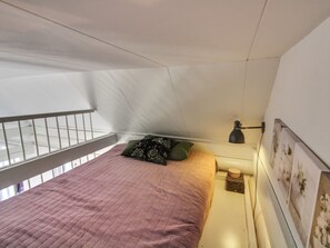 Una camera da letto con un letto, cuscini, un comodino, una lampada e un quadro appeso al muro.