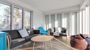 Una sala moderna con un sofá gris, una silla azul, un sillón de pelota marrón y una mesa de centro redonda de madera.