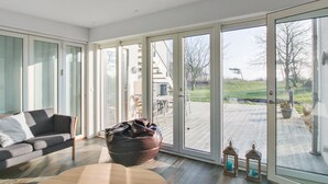Una sala moderna con sofá, sillón de peluche y vistas a una terraza y zona exterior.