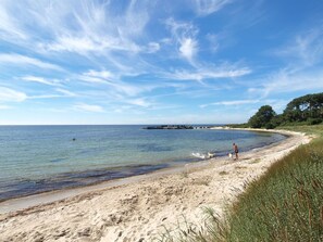 Une plage avec un ciel dégagé, une eau calme et une jetée qui se dessine à l’horizon.