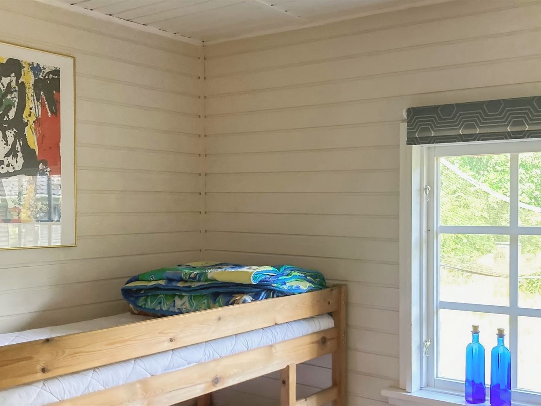 Una habitación con literas, una ventana con vista a follaje y una obra de arte enmarcada en la pared.