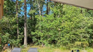 Une terrasse en bois avec deux chaises longues, une table avec une bouteille et des verres, et une vue sur une zone boisée.