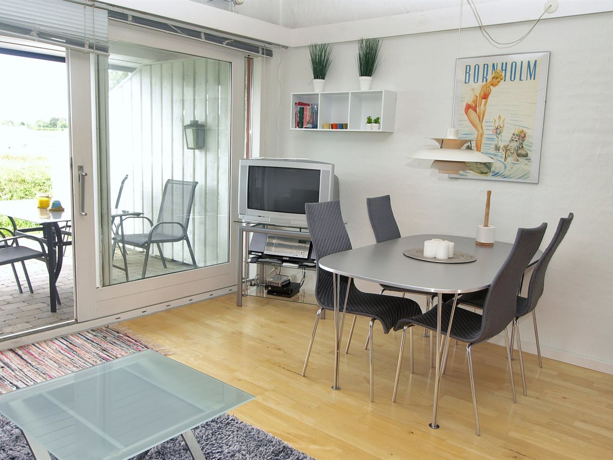 Una sala de estar moderna con una mesa de centro de vidrio, una mesa de comedor con sillas, un televisor y una estantería.
