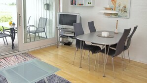 Un salon moderne avec une table basse en verre, une table à manger avec des chaises, un téléviseur et une bibliothèque.