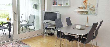 Una sala de estar moderna con una mesa de centro de vidrio, una mesa de comedor con sillas, un televisor y una estantería.