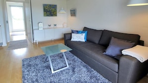 Un salon moderne avec un canapé gris, une table basse en verre et un tapis bleu.
