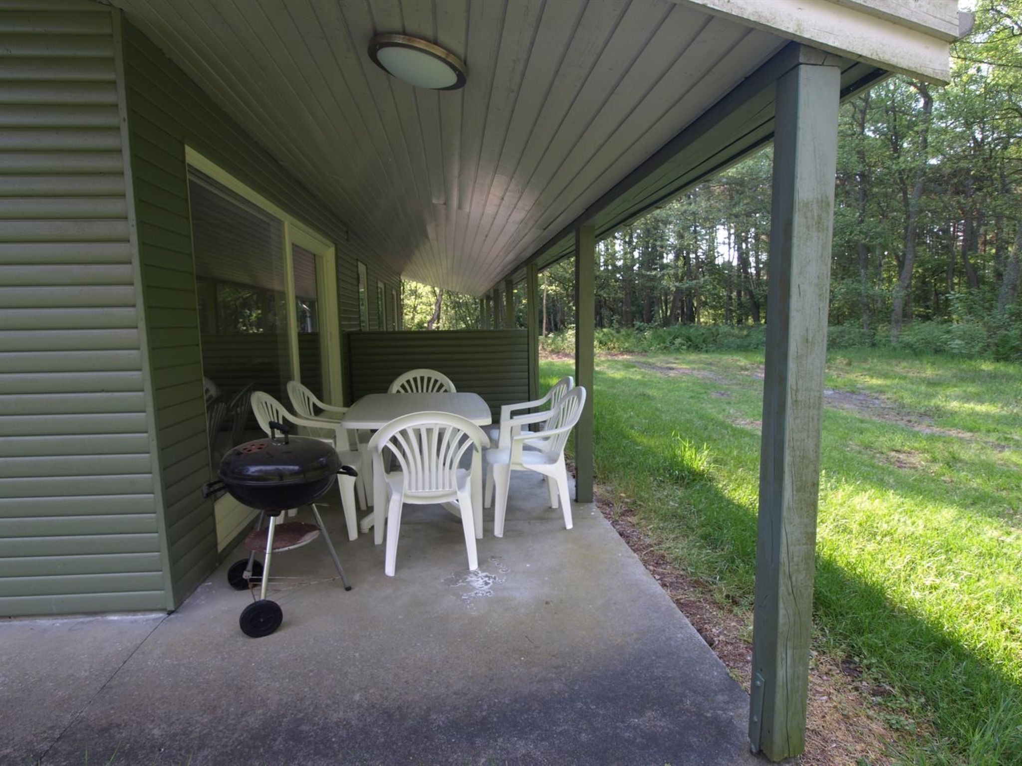A covered patio with a table and chairs, a grill, and a concrete floor.