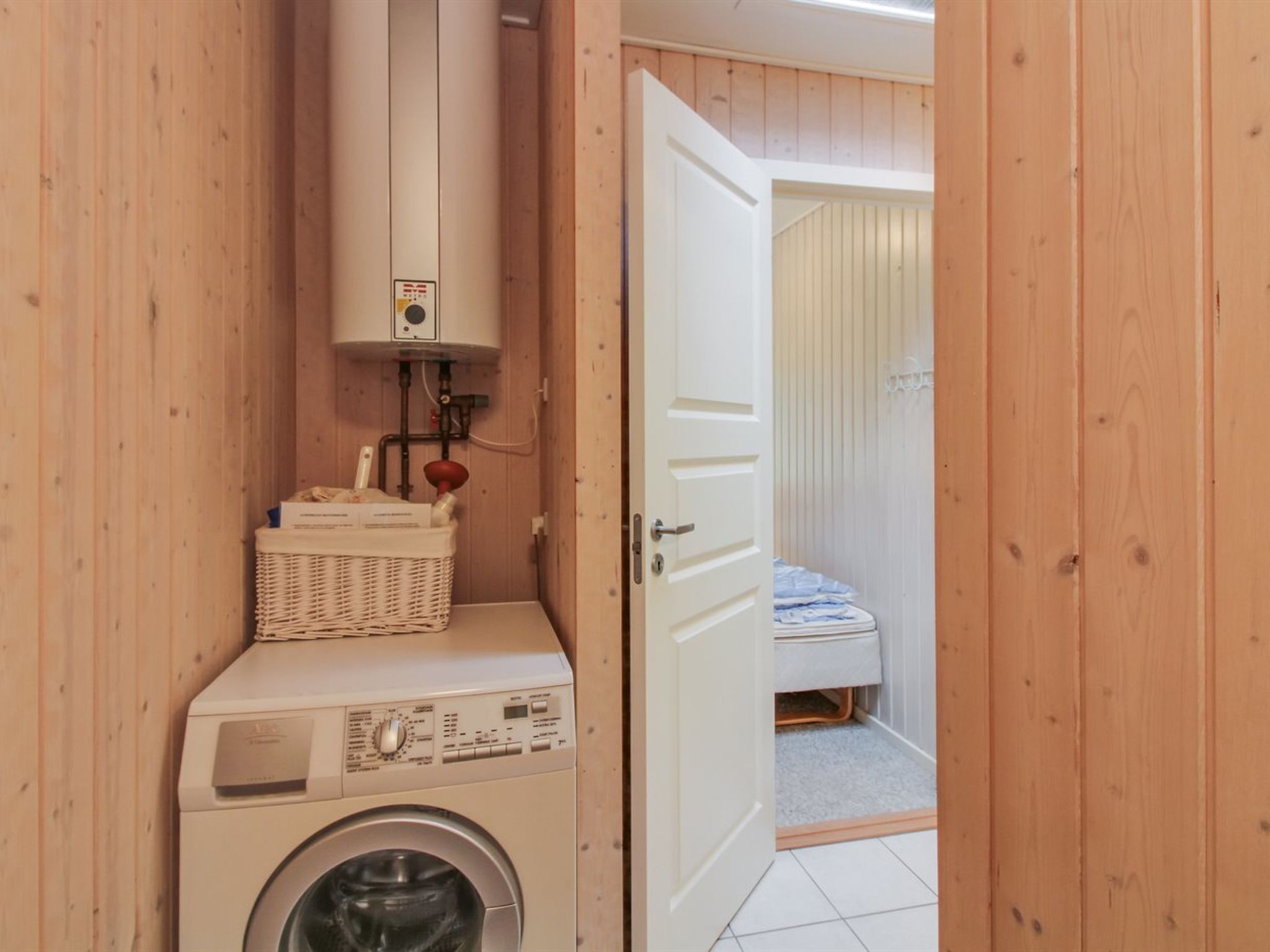 A compact laundry room with a washing machine and a dryer, a white door leading to a bedroom, and a small wicker basket on the dryer.