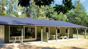 A covered outdoor seating area with tables and chairs, a barbecue grill, and a large sliding glass door entrance.
