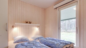 A bedroom with two beds, wooden walls, a window, and a shelf with decorative items.