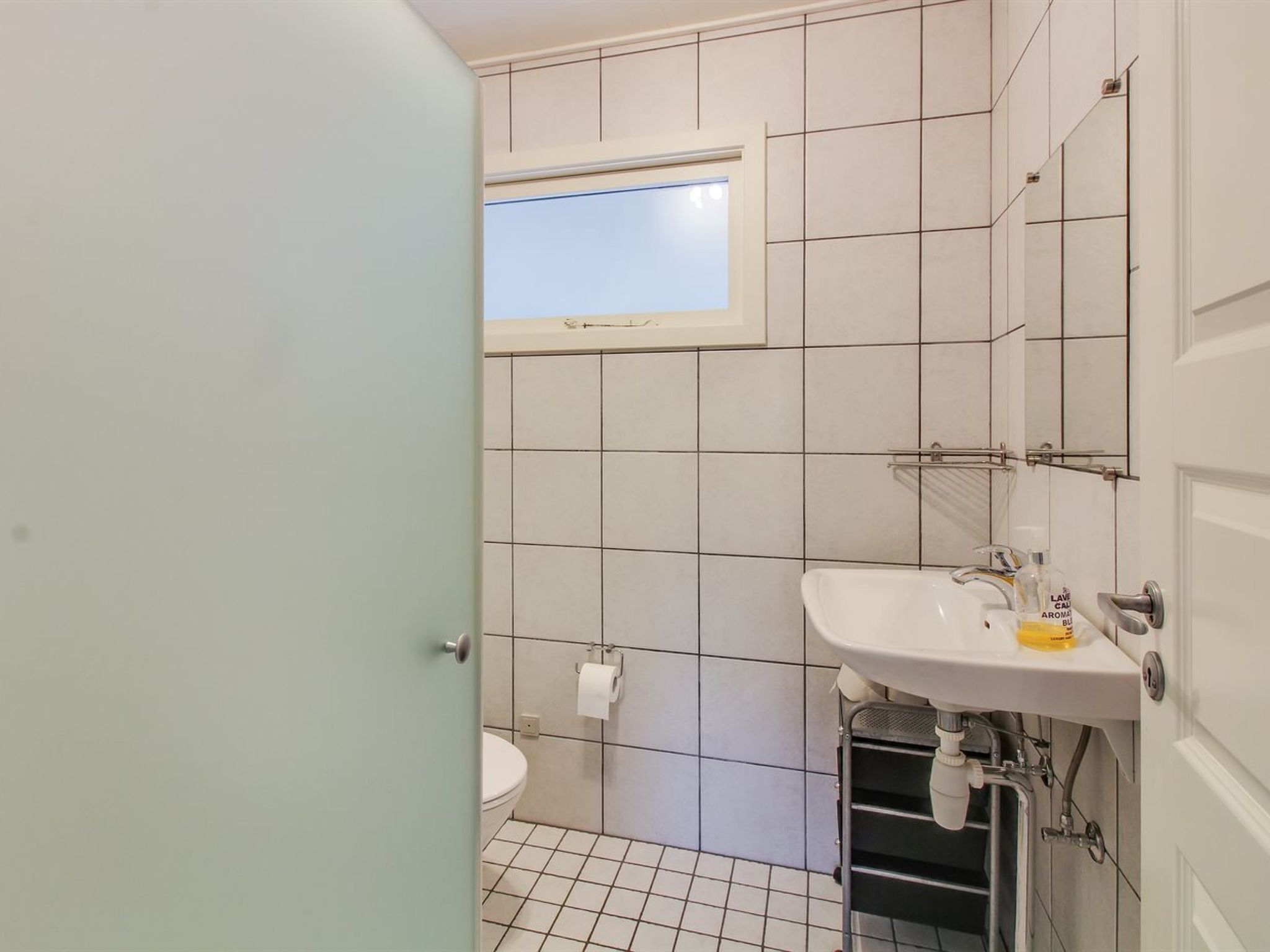 Une petite salle de bain avec des toilettes, un lavabo et une fenêtre située au-dessus des toilettes.